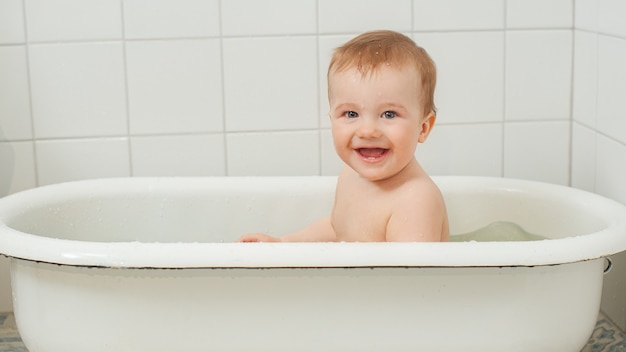 Il piccolo bambino felice fa il bagno in una vasca da bagno