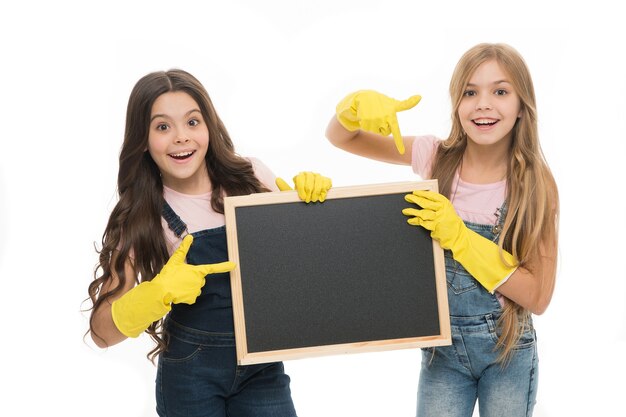 A little help for keeping things tidy. Adorable tidy schoolgirls in rubber gloves pointing at tidy blackboard. Primary school children keeping their school supplies clean and tidy, copy space.