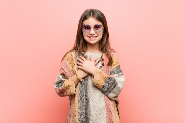 Little hippie girl has friendly expression, pressing palm to chest.