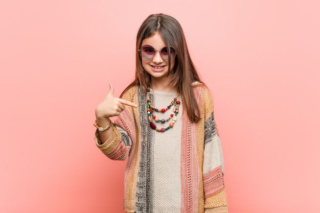 Little hippie girl person pointing by hand to a shirt copy space, proud and confident