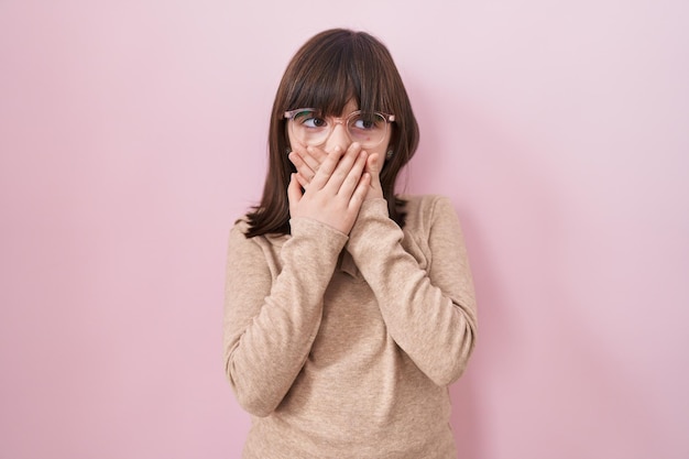 Little hispanic girl wearing glasses shocked covering mouth with hands for mistake secret concept