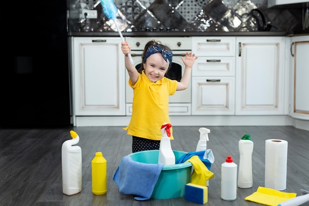 A little housewife with a dusty brush and detergents in the kitchen