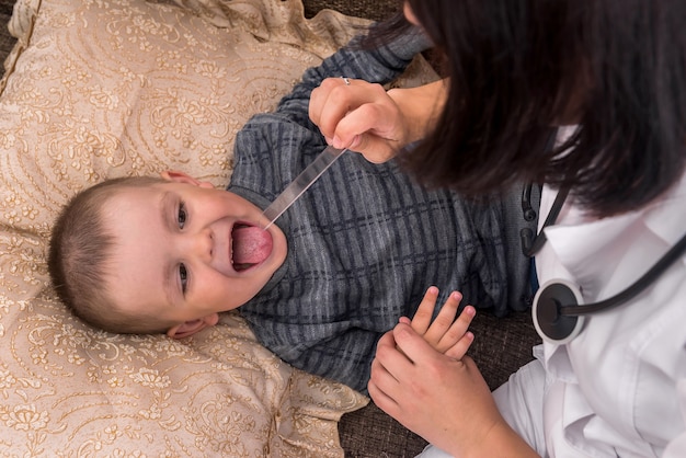 Little ill boy lying on pillow and showing throat to doctor