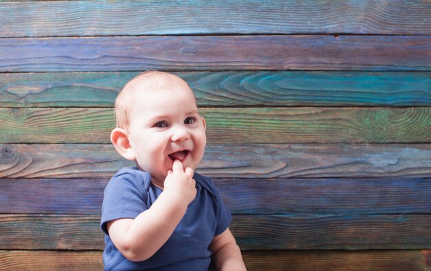 Little joyful boy with his finger in his mouth on a color wooden background