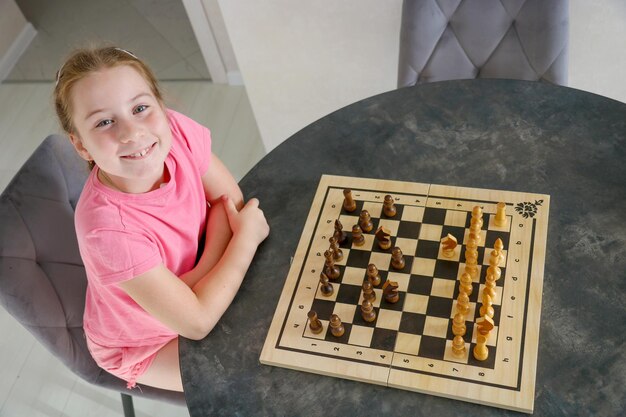 little joyful girl at the table playing chess