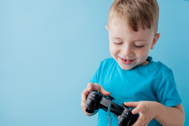 Little kid boy 2-3 years old wearing blue clothes hold in hand joystick for gameson blue background children studio portrait. People childhood lifestyle concept. Mock up copy space