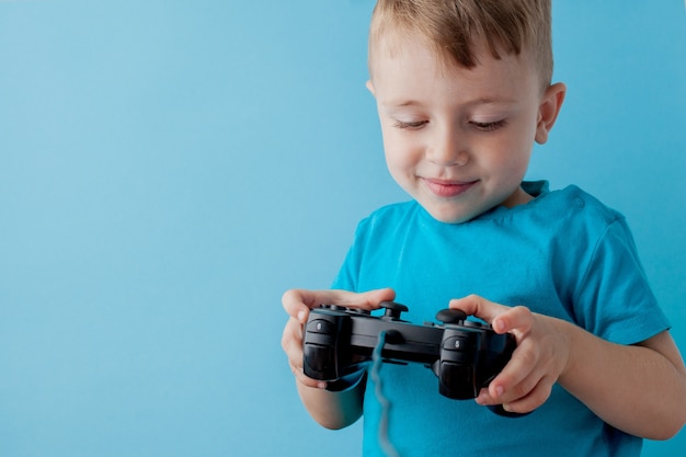 Photo little kid boy 2-3 years old wearing blue clothes hold in hand joystick for gameson blue background children studio portrait.