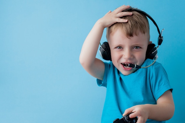 Little kid boy 2-3 years old wearing blue clothes hold in hand joystick for gameson blue children studio portrait. People childhood lifestyle concept. Mock up copy space.