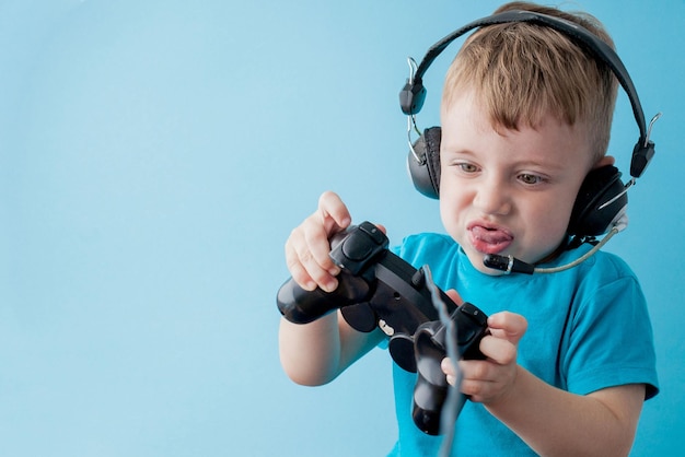 Little kid boy 23 years old wearing blue clothes hold in hand joystick for gameson blue background children studio portrait People childhood lifestyle concept Mock up copy space