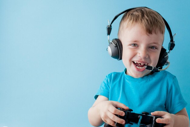 Little kid boy 23 years old wearing blue clothes hold in hand joystick for gameson blue background children studio portrait People childhood lifestyle concept Mock up copy space