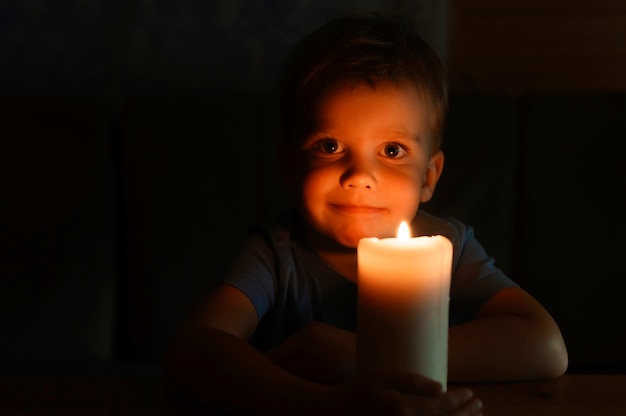 Little kid boy of four years old admires a burning wax candle in the evening at home