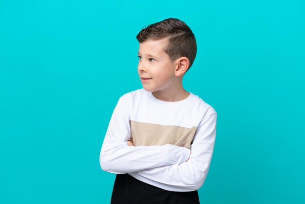 Little kid boy isolated on blue background looking to the side
