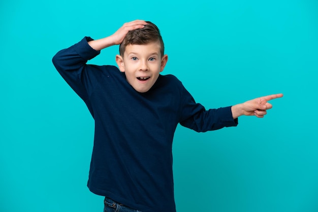 Little kid boy isolated on blue background surprised and pointing finger to the side