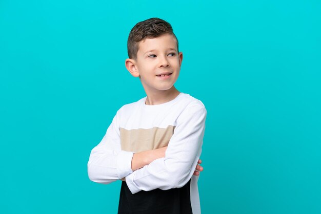 Little kid boy isolated on blue background with arms crossed and happy