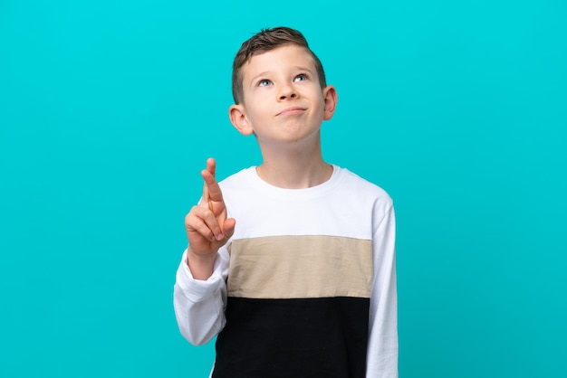 Little kid boy isolated on blue background with fingers crossing and wishing the best