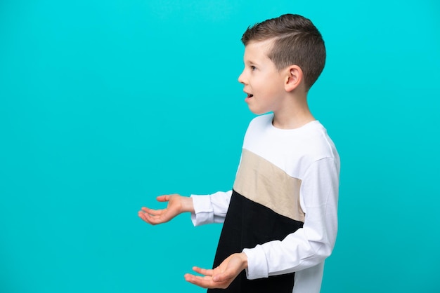 Little kid boy isolated on blue background with surprise expression while looking side