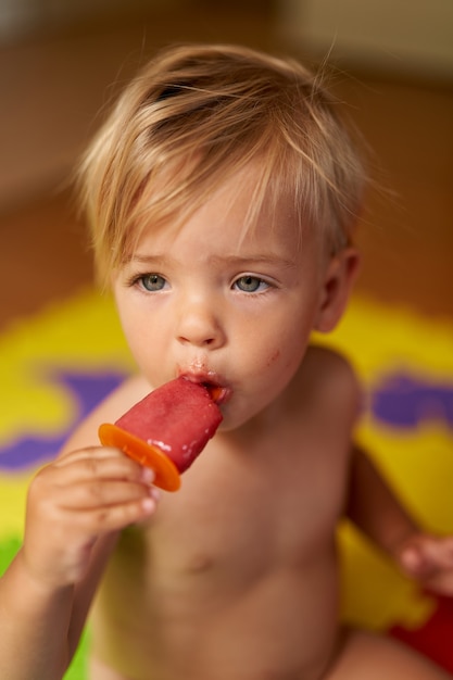 Little kid eats ice cream while sitting on the floor in the room