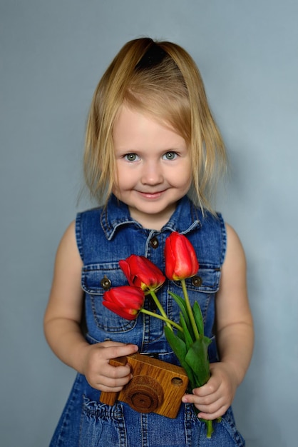 Bambina di quattro anni con tulipani e macchina fotografica in legno giocattolo