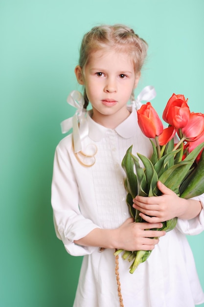 Little kid girl holding red tulips Wearing stylish dress Looking at camera