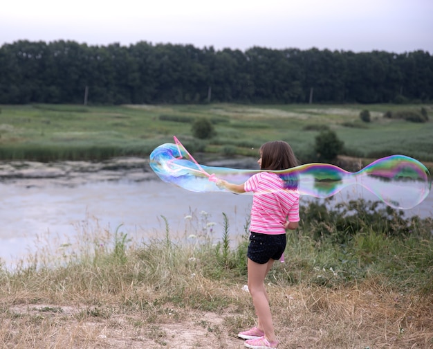 La bambina lancia enormi bolle di sapone sullo sfondo della bellissima natura.