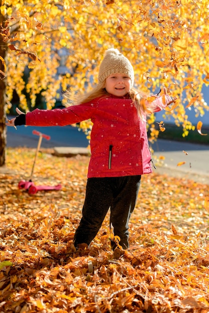 little kid girl playing with leaves in autumn park