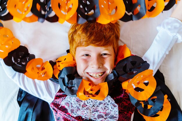 Little kid at home dressed as a vampire for Halloween costume party playing with pumpkin decoration