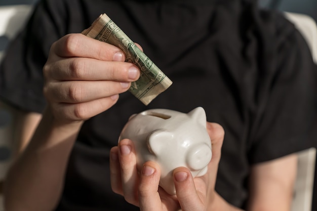 Little kid investor putting his first us dollar into piggy bank.