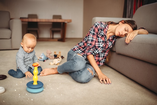 Little kid playing on the floor, mother sleeps