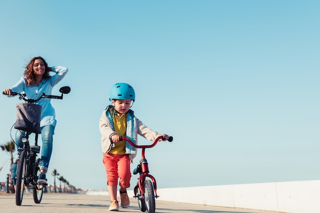 Little kid riding a balance bike with his mother on a bicycle in a city park