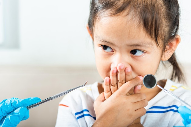 Little kid scared and closes his mouth with hands doctor examines oral cavity