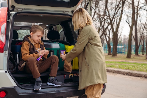 チョコレート菓子を食べる荷物でいっぱいの車のトランクに母親と一緒に座っている小さな子供