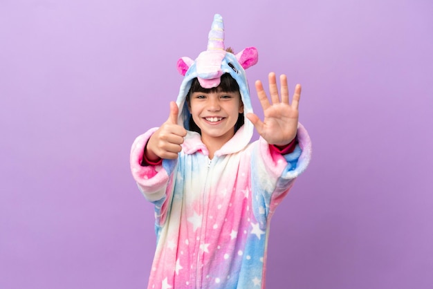 Little kid wearing a unicorn pajama isolated on purple background counting six with fingers