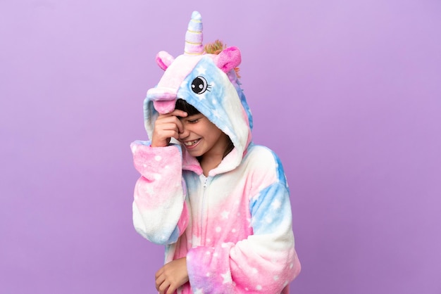 Маленький ребенок в пижаме с единорогом на фиолетовом фоне смеется