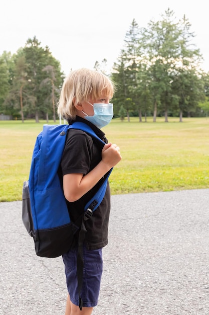 Foto il bambino indossa una maschera e porta uno zaino per andare a scuola.