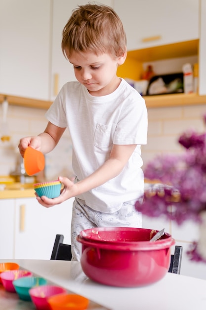 小さな子供は家の軽いキッチンでカップケーキを調理します小さな男の子はシリコーンのベーキング型を使用します