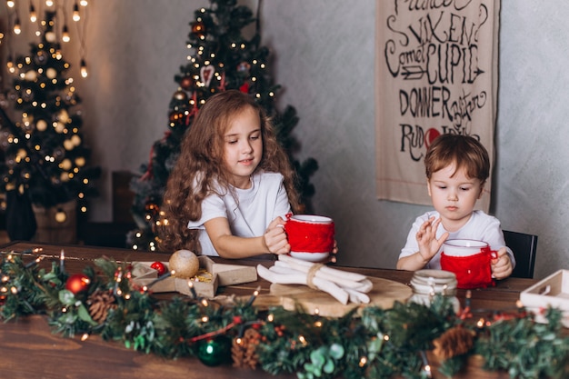 Little kids in christmas decoration with tea at cozy home with colorful new year lights