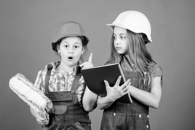 Little kids in helmet with tablet and roller Labor day 1 may small girls repairing together in workshop Foreman inspector Repair engineering idea my idea is perfect let me introduce my idea