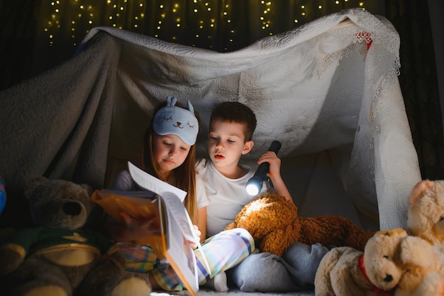 Photo little kids involving in reading amazing book they lying in nice toy tent in playroom boy holding flashlight in hand