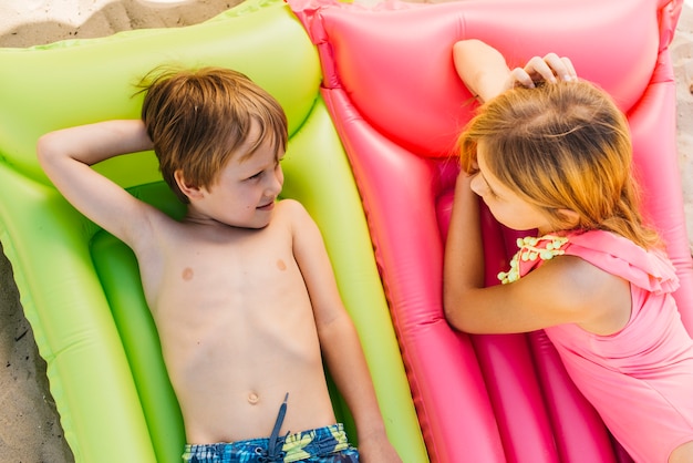 Little kids relaxing on air mattresses on beach