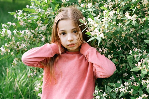 little kind girl in a pink velor suit in the spring in the park near a flowering bush with  flowers