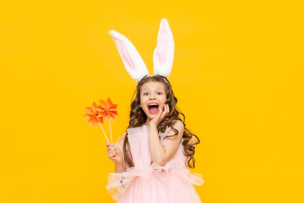 The little lady is celebrating Easter A beautiful little girl with curly hair is enjoying the spring holiday A child with rabbit ears on his head on a yellow isolated background