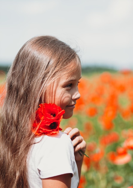 Little longhaired girl posing at field of poppies with on summer sun Vertical