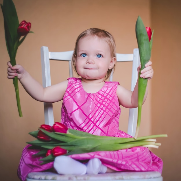 Little lovely baby girl in a pink dress with tulip flowers.  