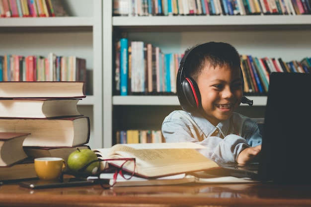 Piccolo adorabile studente straniero che impara, usando il computer con divertimento e felicità.