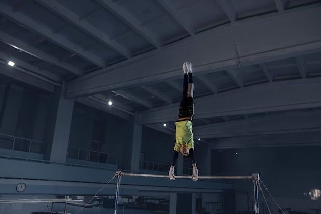 Piccolo ginnasta maschio che si allena in palestra, flessibile e attivo. ragazzino in forma caucasica, atleta in abbigliamento sportivo che pratica esercizi per forza, equilibrio. movimento, azione, movimento, concetto dinamico.