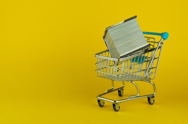 Little metallic cart and a tiny book on a yellow surface and background - copy space