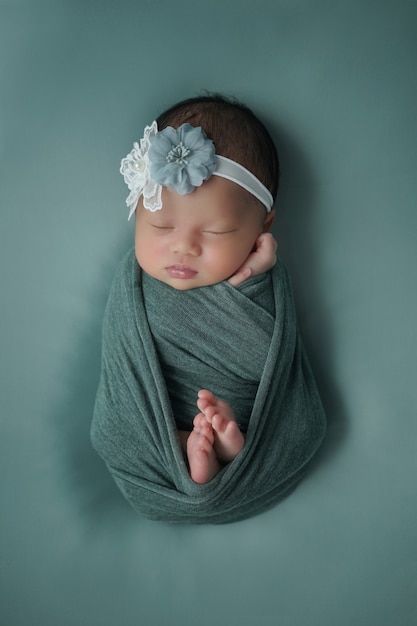 Little newborn baby enveloped in blue scarf with a bandage on his head lies on a soft blanket