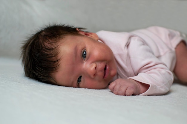 Little newborn baby girl with long hair in pink clothes lies on a white bedspread