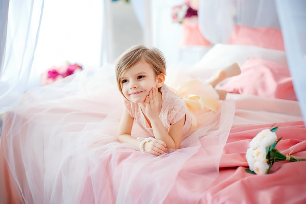 Little nice girl in dress lying on bed with flowers