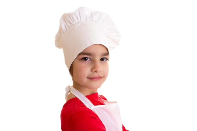 Маленькая симпатичная девочка в красной рубашке с белым фартуком и белой шляпой на белом фоне